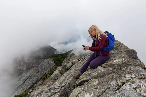 Genç Maceracı Kız bulutlu bir yaz sabahı bir selfie alarak engebeli kayalık dağın tepesinde. Crown Mountain'da çekilmiş, Kuzey Vancouver, Bc, Kanada.