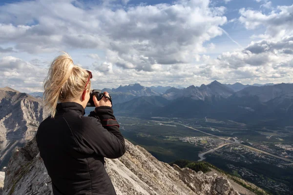 Macera kadın Fotoğrafçı bulutlu bir gün boyunca kayalık bir dağın tepesinde fotoğraf çekiyor. Lady Macdonald, Canmore, Alberta, Kanada'dan alındı.