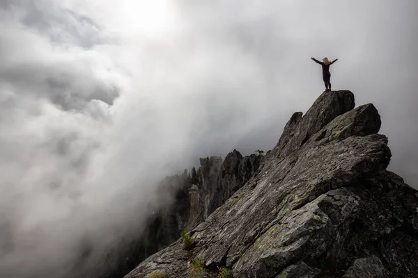 Bulutlu bir yaz sabahı engebeli kayalık dağın tepesinde Açık Kollu Maceracı Kız. Crown Mountain'da çekilmiş, Kuzey Vancouver, Bc, Kanada.