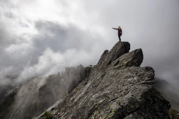 Maceracı Kız bulutlu bir yaz sabahı boyunca engebeli kayalık dağın üstüne parmak işaret. Crown Mountain'da çekilmiş, Kuzey Vancouver, Bc, Kanada.