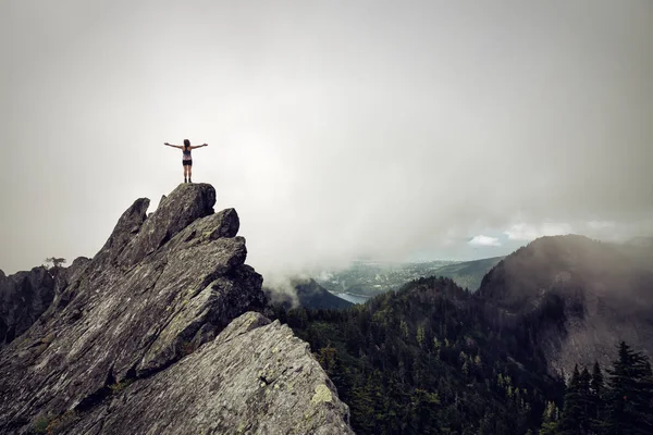 Bulutlu bir yaz sabahı engebeli kayalık dağın tepesinde Açık Kollu Maceracı Kız. Crown Mountain'da çekilmiş, Kuzey Vancouver, Bc, Kanada.