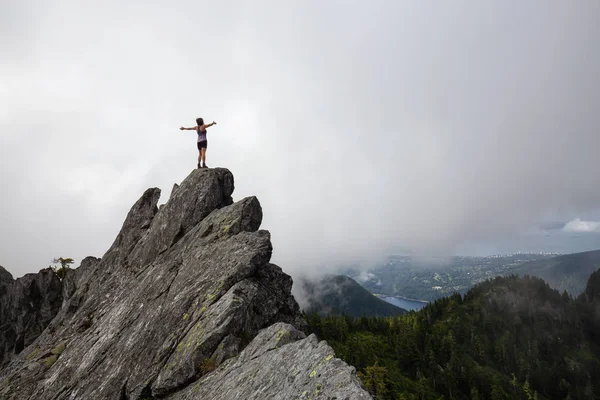 Bulutlu bir yaz sabahı engebeli kayalık dağın tepesinde Açık Kollu Maceracı Kız. Crown Mountain'da çekilmiş, Kuzey Vancouver, Bc, Kanada.