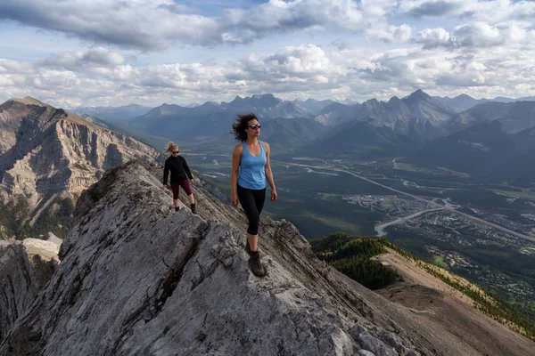 Adventurous Girl is hiking up a rocky mountain during a cloudy and rainy day. Taken from Mt Lady MacDonald, Canmore, Alberta, Canada.