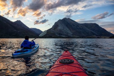 Buzul Gölü 'nde Maceracı Adam Kayağı bulutlu yaz günbatımında güzel Kanada Rocky Dağları ile çevrili. Yukarı Waterton Gölü, Alberta, Kanada.