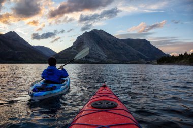 Buzul Gölü 'nde Maceracı Adam Kayağı bulutlu yaz günbatımında güzel Kanada Rocky Dağları ile çevrili. Yukarı Waterton Gölü, Alberta, Kanada.