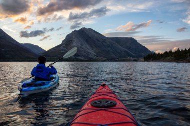 Buzul Gölü 'nde Maceracı Adam Kayağı bulutlu yaz günbatımında güzel Kanada Rocky Dağları ile çevrili. Yukarı Waterton Gölü, Alberta, Kanada.