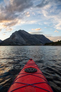 Buzul Gölü 'nde kayak yaparken bulutlu bir yaz günbatımında güzel Kanada Rocky Dağları etrafını sarmıştı. Yukarı Waterton Gölü, Alberta, Kanada.