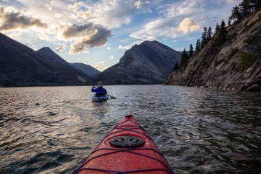 Buzul Gölü 'nde Maceracı Adam Kayağı bulutlu yaz günbatımında güzel Kanada Rocky Dağları ile çevrili. Yukarı Waterton Gölü, Alberta, Kanada.