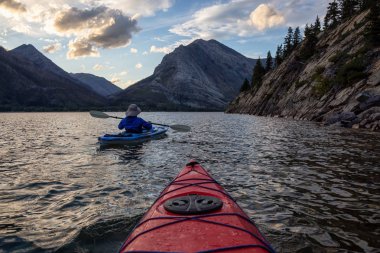 Buzul Gölü 'nde Maceracı Adam Kayağı bulutlu yaz günbatımında güzel Kanada Rocky Dağları ile çevrili. Yukarı Waterton Gölü, Alberta, Kanada.