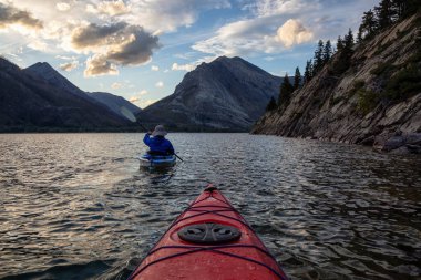 Buzul Gölü 'nde Maceracı Adam Kayağı bulutlu yaz günbatımında güzel Kanada Rocky Dağları ile çevrili. Yukarı Waterton Gölü, Alberta, Kanada.