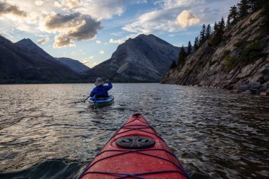 Buzul Gölü 'nde Maceracı Adam Kayağı bulutlu yaz günbatımında güzel Kanada Rocky Dağları ile çevrili. Yukarı Waterton Gölü, Alberta, Kanada.