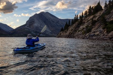 Buzul Gölü 'nde Maceracı Adam Kayağı bulutlu yaz günbatımında güzel Kanada Rocky Dağları ile çevrili. Yukarı Waterton Gölü, Alberta, Kanada.