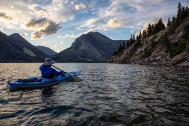 Buzul Gölü 'nde Maceracı Adam Kayağı bulutlu yaz günbatımında güzel Kanada Rocky Dağları ile çevrili. Yukarı Waterton Gölü, Alberta, Kanada.