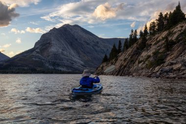 Buzul Gölü 'nde Maceracı Adam Kayağı bulutlu yaz günbatımında güzel Kanada Rocky Dağları ile çevrili. Yukarı Waterton Gölü, Alberta, Kanada.
