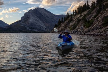 Buzul Gölü 'nde Maceracı Adam Kayağı bulutlu yaz günbatımında güzel Kanada Rocky Dağları ile çevrili. Yukarı Waterton Gölü, Alberta, Kanada.