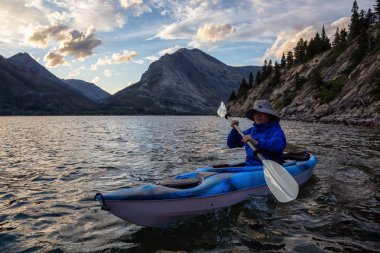 Buzul Gölü 'nde Maceracı Adam Kayağı bulutlu yaz günbatımında güzel Kanada Rocky Dağları ile çevrili. Yukarı Waterton Gölü, Alberta, Kanada.
