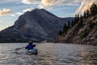 Buzul Gölü 'nde Maceracı Adam Kayağı bulutlu yaz günbatımında güzel Kanada Rocky Dağları ile çevrili. Yukarı Waterton Gölü, Alberta, Kanada.