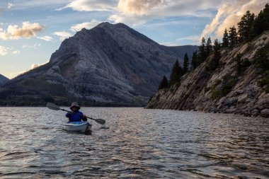 Buzul Gölü 'nde Maceracı Adam Kayağı bulutlu yaz günbatımında güzel Kanada Rocky Dağları ile çevrili. Yukarı Waterton Gölü, Alberta, Kanada.