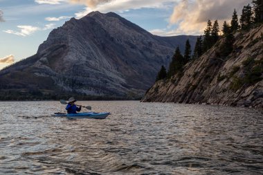 Buzul Gölü 'nde Maceracı Adam Kayağı bulutlu yaz günbatımında güzel Kanada Rocky Dağları ile çevrili. Yukarı Waterton Gölü, Alberta, Kanada.