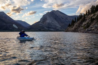 Buzul Gölü 'nde Maceracı Adam Kayağı bulutlu yaz günbatımında güzel Kanada Rocky Dağları ile çevrili. Yukarı Waterton Gölü, Alberta, Kanada.