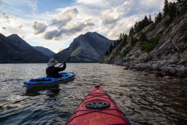 Buzul Gölü 'nde Maceracı Adam Kayağı bulutlu yaz günbatımında güzel Kanada Rocky Dağları ile çevrili. Yukarı Waterton Gölü, Alberta, Kanada.