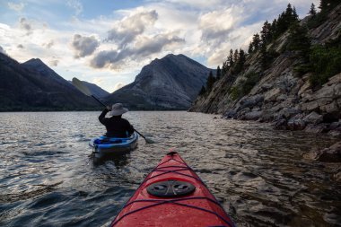 Buzul Gölü 'nde Maceracı Adam Kayağı bulutlu yaz günbatımında güzel Kanada Rocky Dağları ile çevrili. Yukarı Waterton Gölü, Alberta, Kanada.