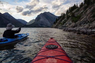 Buzul Gölü 'nde Maceracı Adam Kayağı bulutlu yaz günbatımında güzel Kanada Rocky Dağları ile çevrili. Yukarı Waterton Gölü, Alberta, Kanada.