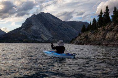 Buzul Gölü 'nde Maceracı Adam Kayağı bulutlu yaz günbatımında güzel Kanada Rocky Dağları ile çevrili. Yukarı Waterton Gölü, Alberta, Kanada.