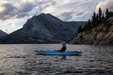 Buzul Gölü 'nde Maceracı Adam Kayağı bulutlu yaz günbatımında güzel Kanada Rocky Dağları ile çevrili. Yukarı Waterton Gölü, Alberta, Kanada.