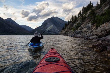 Buzul Gölü 'nde Maceracı Adam Kayağı bulutlu yaz günbatımında güzel Kanada Rocky Dağları ile çevrili. Yukarı Waterton Gölü, Alberta, Kanada.