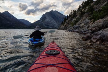 Buzul Gölü 'nde Maceracı Adam Kayağı bulutlu yaz günbatımında güzel Kanada Rocky Dağları ile çevrili. Yukarı Waterton Gölü, Alberta, Kanada.
