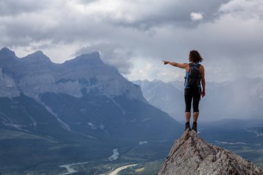 Maceracı Kafkas Kız bulutlu ve yağmurlu bir gün boyunca kayalık bir dağın üstüne bir parmak işaret. Lady Macdonald, Canmore, Alberta, Kanada'dan alındı.