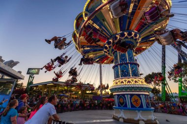 Vancouver, British Columbia, Kanada - 25 Ağustos 2019: Çocuklar canlı bir yaz gün batımı nda Pne'de salıncak atlıkarınca yolculuğunda eğleniyor.