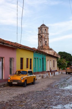 Trinidad, Küba - 12 Haziran 2019: Canlı güneşli bir gün batımında arka planda Kilise ile küçük bir Küba Kasabası sokaklarında eski bir Klasik Taksi Arabası Görünümü.
