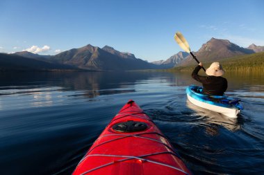 Maceraperest Adam McDonald Gölü 'nde güneşli bir yaz akşamında arka planda Amerikan Rocky Dağları ile kayak yapıyor. Buzul Ulusal Parkı, Montana, ABD 'de çekildi..