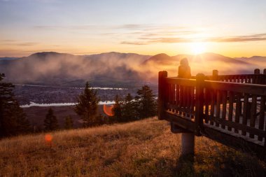 Girl Standing on a Lookout and looking at a Beautiful View of a Canadian City, Kamloops, during a colorful summer sunrise. Located in the Interior British Columbia, Canada. clipart
