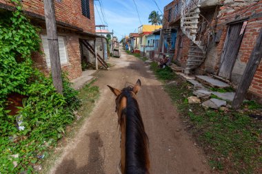 Trinidad, Küba - 12 Haziran 2019: Canlı güneşli bir günde küçük bir Küba Kasabasının sokaklarında bir atın üstüne binmek.