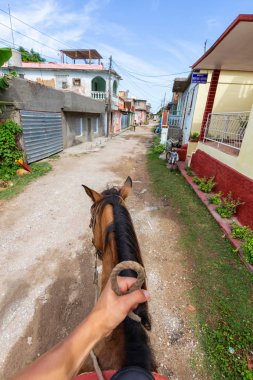 Trinidad, Küba - 12 Haziran 2019: Canlı güneşli bir günde küçük bir Küba Kasabasının sokaklarında bir atın üstüne binmek.