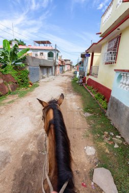 Trinidad, Küba - 12 Haziran 2019: Canlı güneşli bir günde küçük bir Küba Kasabasının sokaklarında bir atın üstüne binmek.