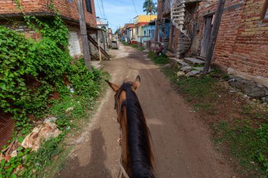Trinidad, Küba - 12 Haziran 2019: Canlı güneşli bir günde küçük bir Küba Kasabasının sokaklarında bir atın üstüne binmek.