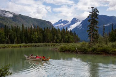Blue River, British Columbia, Kanada - 16 Ağustos 2019: Kanodaki insanlar arka planda Dağlar olan bir gölde tur atıyor.