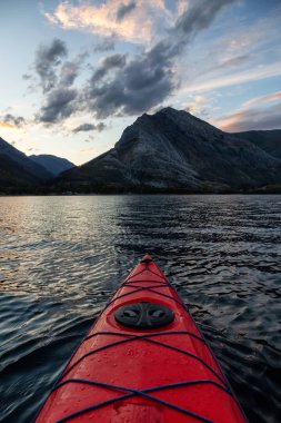 Buzul Gölü 'nde kayak yaparken bulutlu bir yaz günbatımında güzel Kanada Rocky Dağları etrafını sarmıştı. Yukarı Waterton Gölü, Alberta, Kanada.