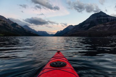 Kayaking in Glacier Lake surrounded by the beautiful Canadian Rocky Mountains during a cloudy summer sunset. Taken in Upper Waterton Lake, Alberta, Canada. clipart