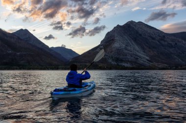 Buzul Gölü 'nde Maceracı Adam Kayağı bulutlu yaz günbatımında güzel Kanada Rocky Dağları ile çevrili. Yukarı Waterton Gölü, Alberta, Kanada.