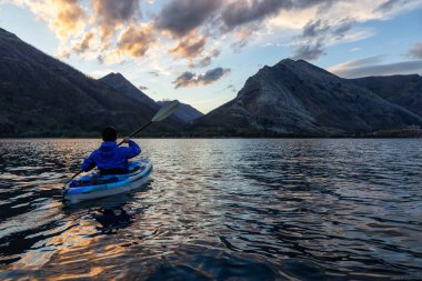 Buzul Gölü 'nde Maceracı Adam Kayağı bulutlu yaz günbatımında güzel Kanada Rocky Dağları ile çevrili. Yukarı Waterton Gölü, Alberta, Kanada.