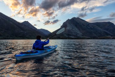 Buzul Gölü 'nde Maceracı Adam Kayağı bulutlu yaz günbatımında güzel Kanada Rocky Dağları ile çevrili. Yukarı Waterton Gölü, Alberta, Kanada.