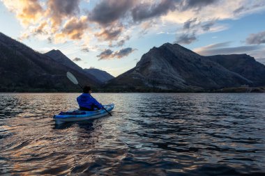 Buzul Gölü 'nde Maceracı Adam Kayağı bulutlu yaz günbatımında güzel Kanada Rocky Dağları ile çevrili. Yukarı Waterton Gölü, Alberta, Kanada.