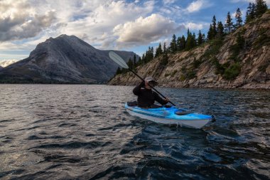 Buzul Gölü 'nde Maceracı Adam Kayağı bulutlu yaz günbatımında güzel Kanada Rocky Dağları ile çevrili. Yukarı Waterton Gölü, Alberta, Kanada.
