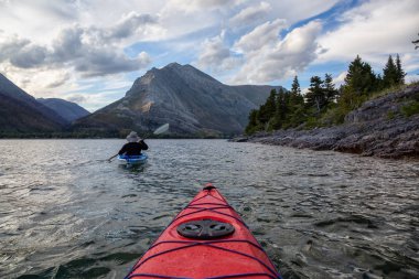 Buzul Gölü 'nde Maceracı Adam Kayağı bulutlu yaz günbatımında güzel Kanada Rocky Dağları ile çevrili. Yukarı Waterton Gölü, Alberta, Kanada.