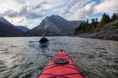 Buzul Gölü 'nde Maceracı Adam Kayağı bulutlu yaz günbatımında güzel Kanada Rocky Dağları ile çevrili. Yukarı Waterton Gölü, Alberta, Kanada.